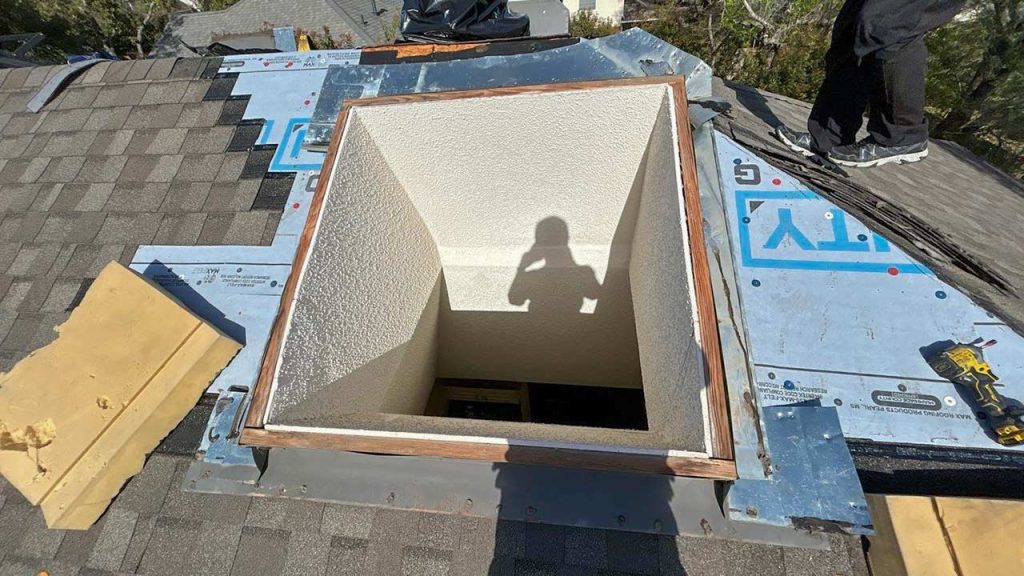 An image of a skylight curb with surrounding shingles removed.