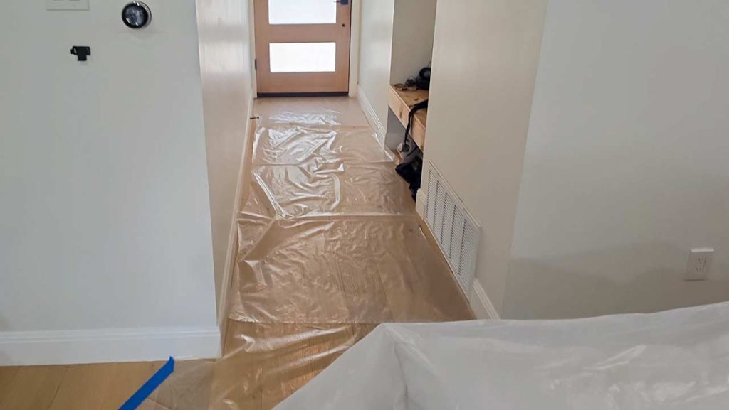 A hallway covered in plastic sheeting for protection, featuring a door at the far end.