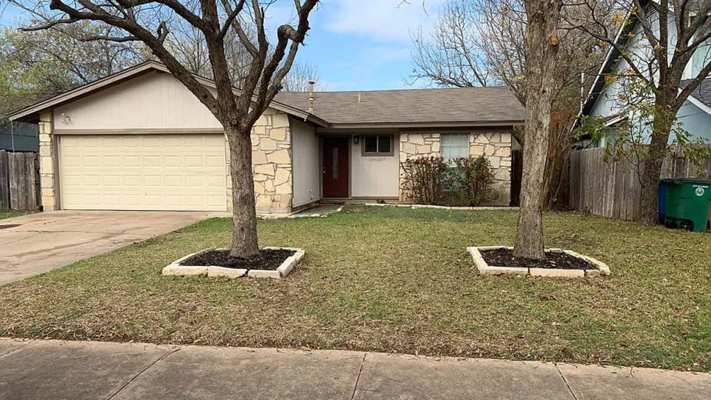 A home featuring a garage, flanked by two trees in a suburban neighborhood.